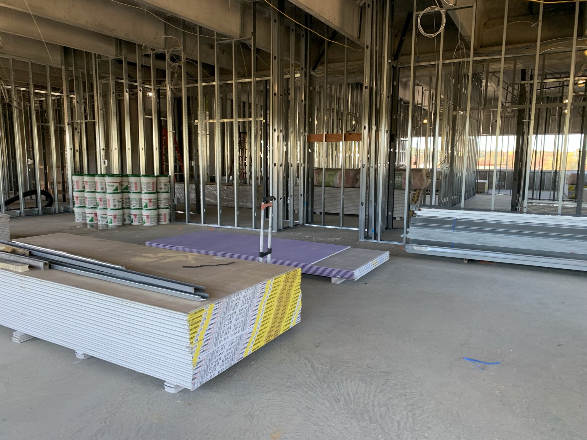 Metal-stud interior framing with stacks of drywall beneath an unfinished concrete ceiling